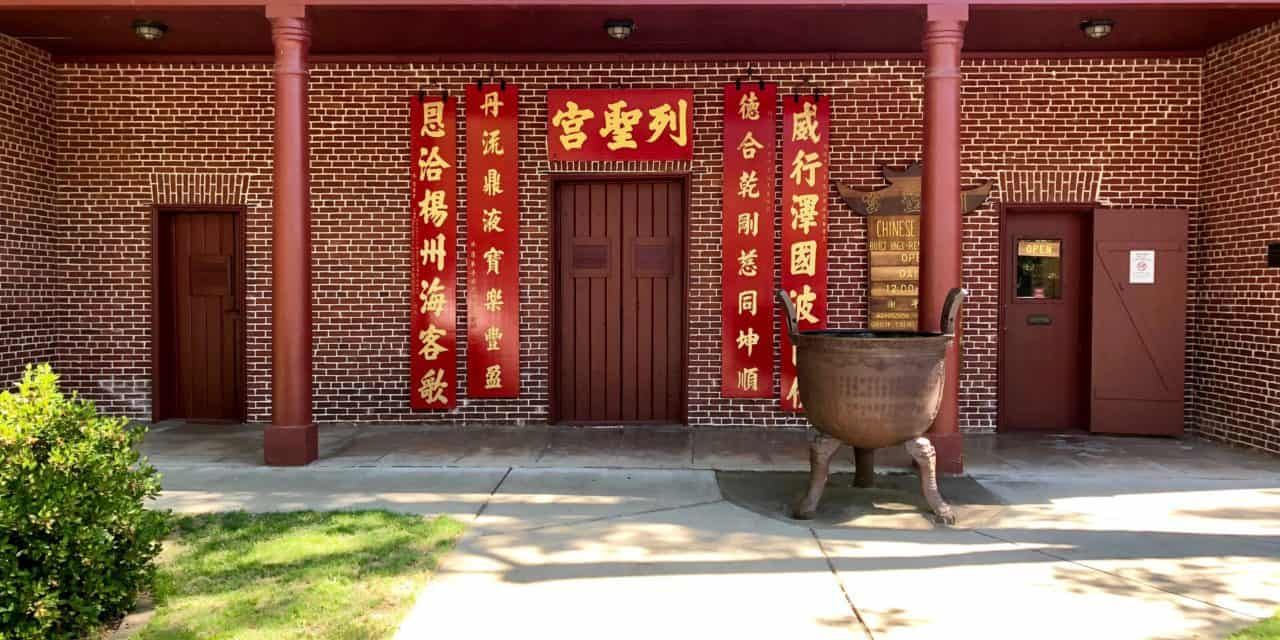 A brick building with chinese writing on it and a large pot in front of it.