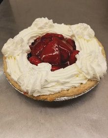 A strawberry pie with whipped cream and strawberries on a table.