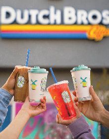 A group of people are holding drinks in front of a dutch bros coffee shop.