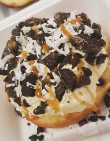 A close up of a pizza with chocolate chips and coconut on a styrofoam container.