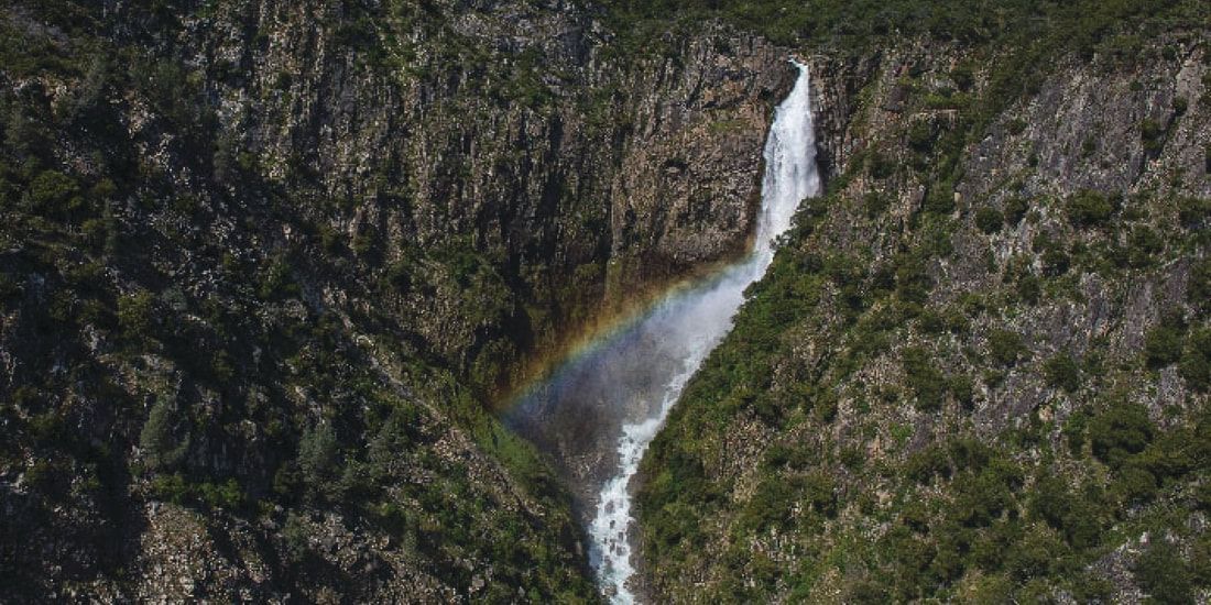 An aerial view of a waterfall with a rainbow in the background.