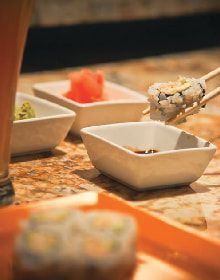 A person is eating sushi with chopsticks from a bowl on a table.