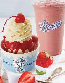 A cup of ice cream with a cherry on top next to a cup of strawberry milkshake.
