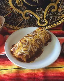 A burrito with cheese and sauce on a white plate on a table.