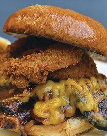 A close up of a chicken sandwich with cheese and onion rings on a bun.