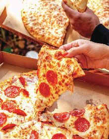 A person is taking a slice of pepperoni pizza out of a box.