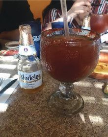 A bottle of modelos beer is next to a large glass of beer.