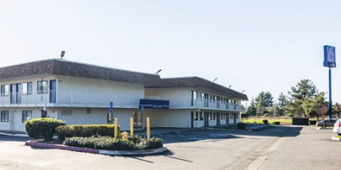 A white motel with a blue sign in front of it.