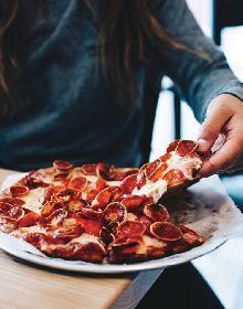 A person is taking a slice of pepperoni pizza from a plate.