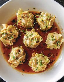 A white plate topped with dumplings and sauce on a table.