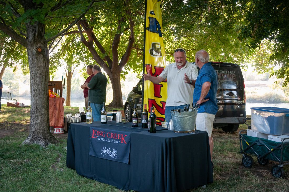 A group of men are standing around a table with bottles of wine on it.