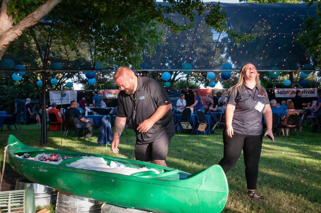 A man and a woman are standing next to a green canoe in a park.