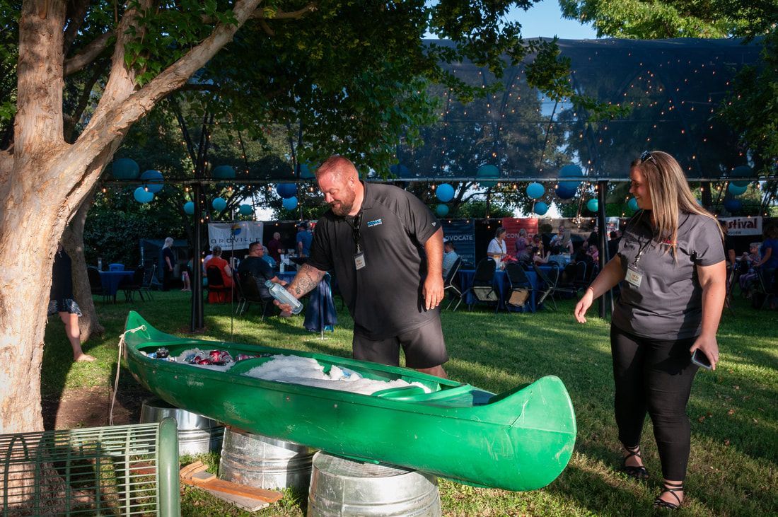 A man and a woman are carrying a green canoe in a park.