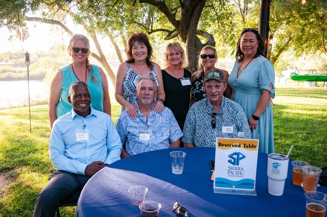 A group of people are sitting around a table in a park.