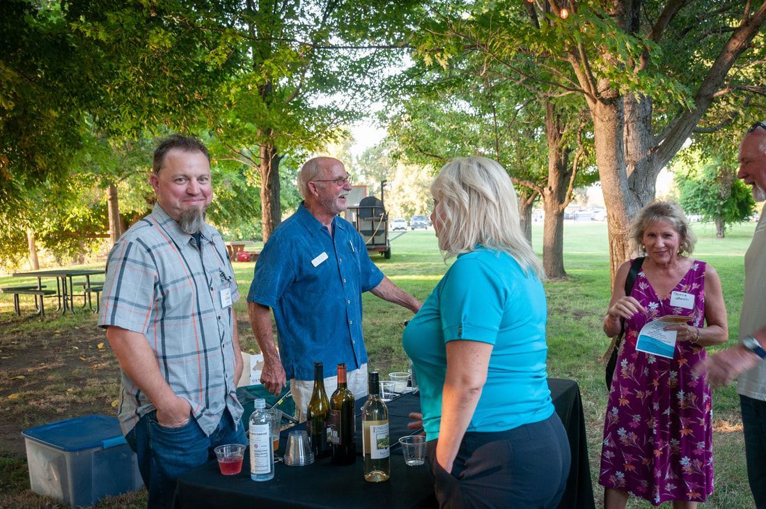 A group of people are standing around a table with bottles of wine.