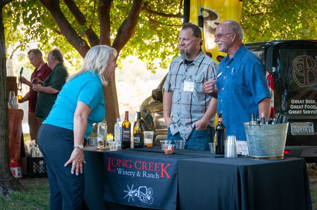 A group of people standing around a long creek wine bar table