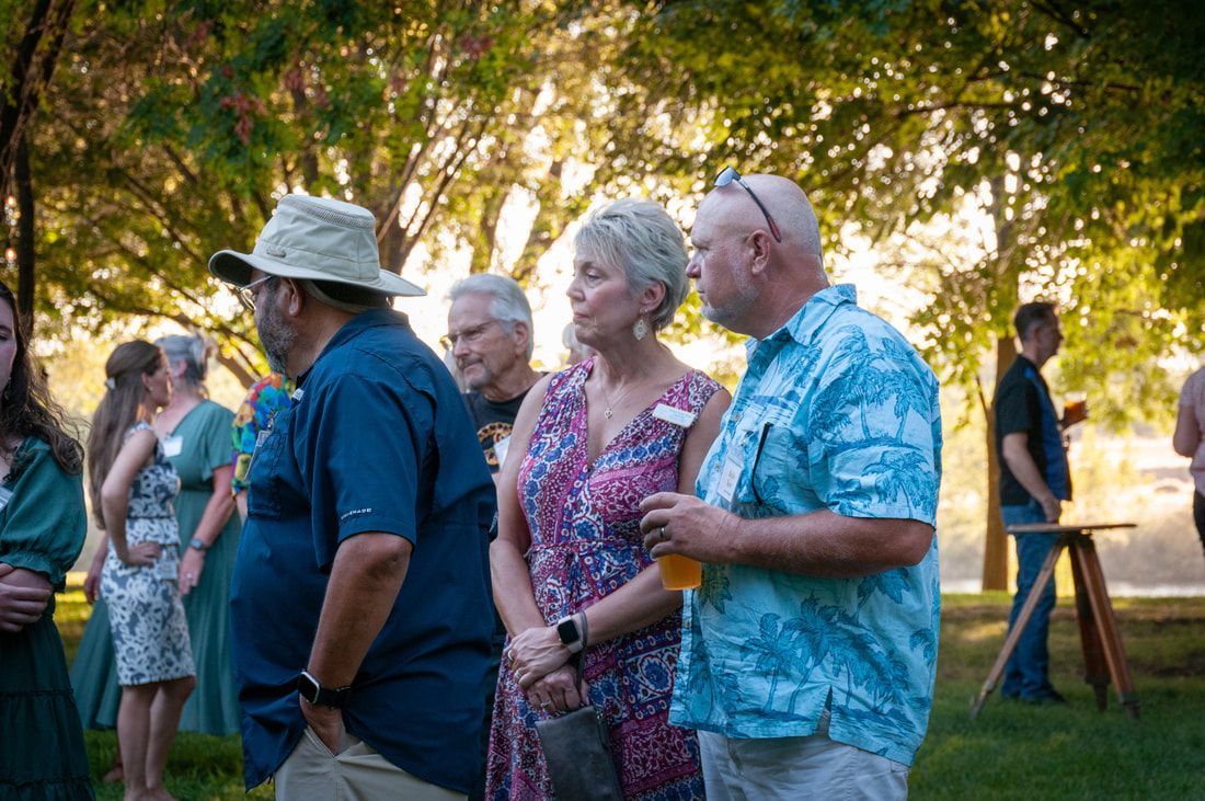 A group of people are standing in the grass talking to each other.