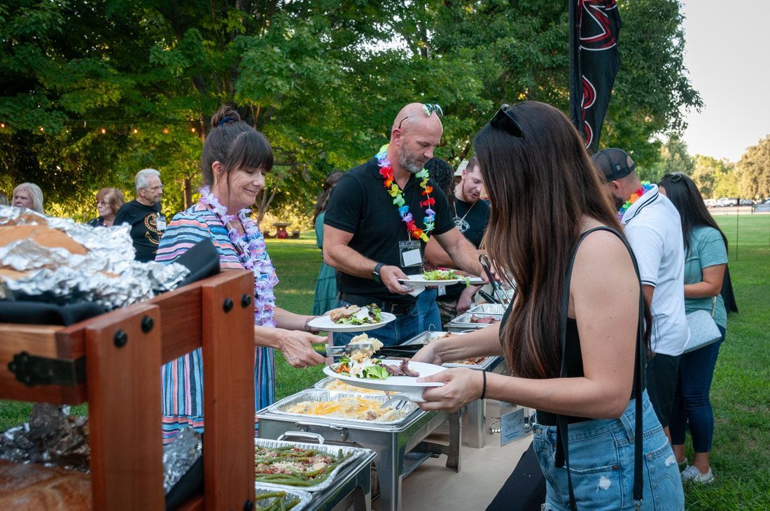 A group of people are standing around a buffet table in a park.