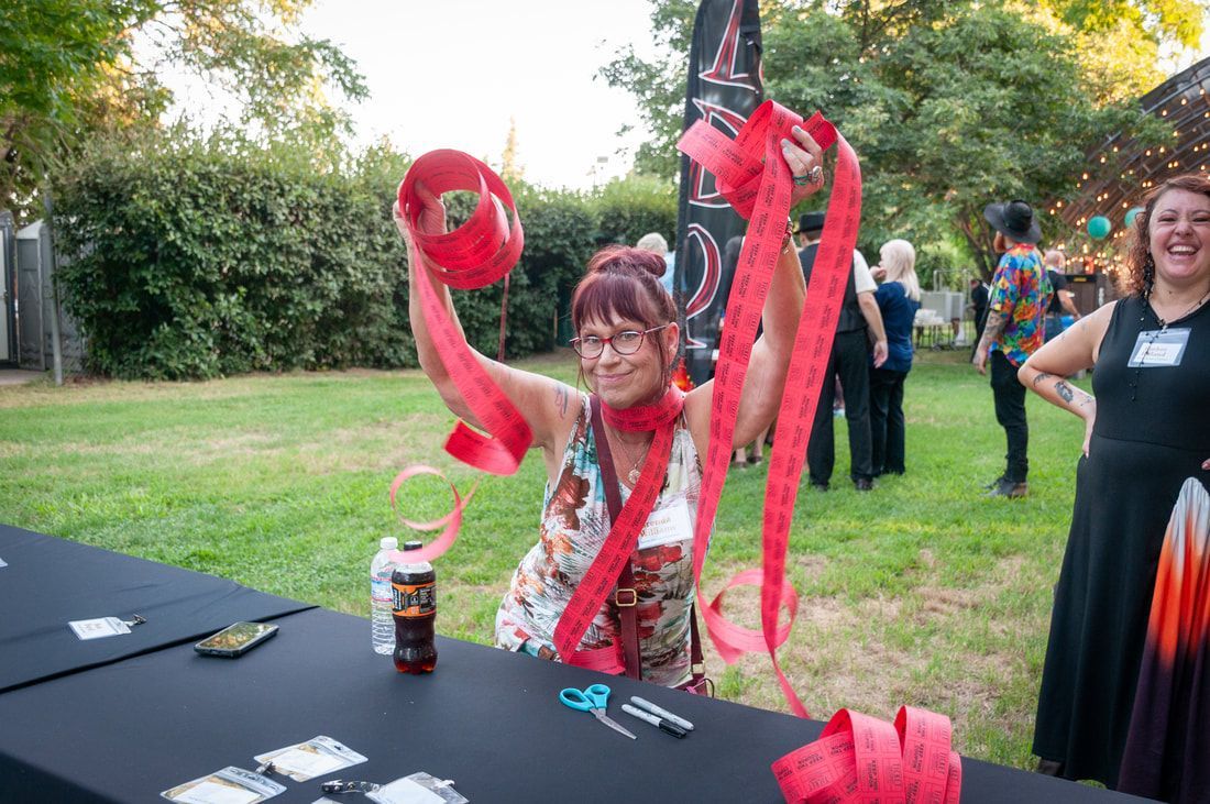A woman is sitting at a table holding a red ribbon.