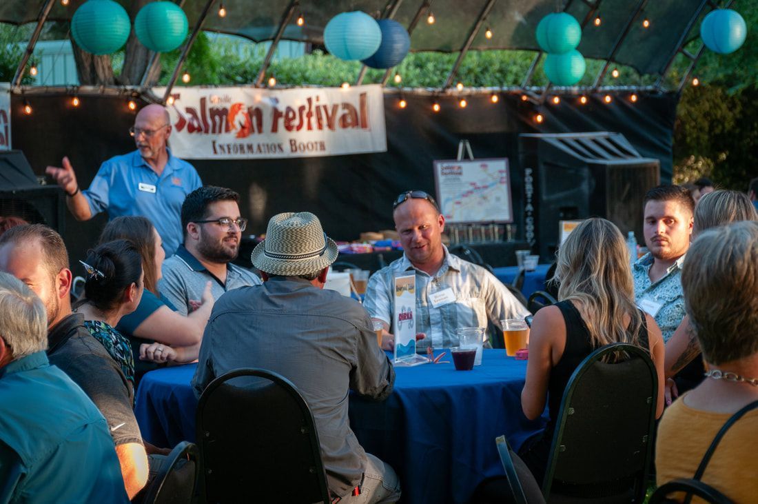 A group of people are sitting around a table at a salmon festival.