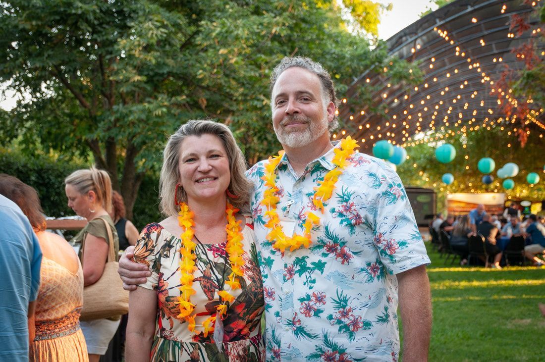 A man and a woman are posing for a picture while wearing lei necklaces.