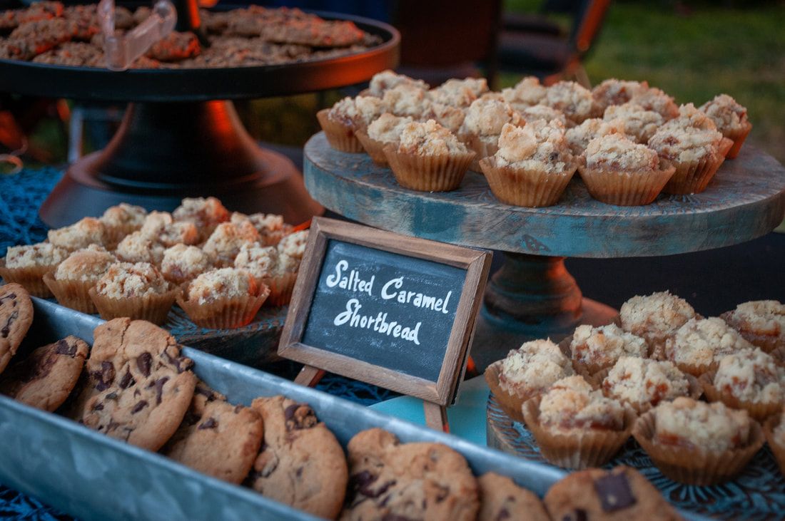 A tray of cookies and muffins on a table with a sign that says sliced caramel shortbread.