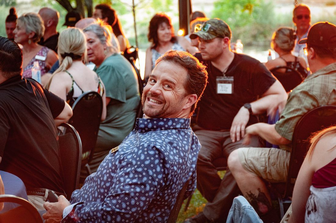 A man is smiling while sitting in a crowd of people.