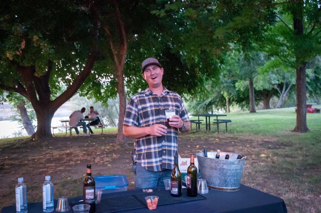 A man is standing in front of a table with bottles of alcohol on it.