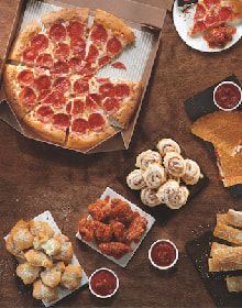 A pizza , chicken nuggets , and other food are on a table.