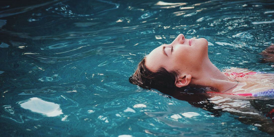 A woman is floating on her back in a swimming pool with her eyes closed.