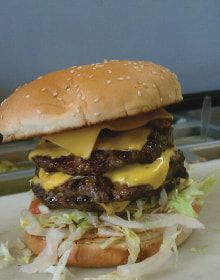 A double cheeseburger with lettuce and onions on a bun on a table.