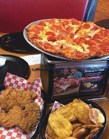A pepperoni pizza is sitting on top of a table next to fried chicken and plantains.