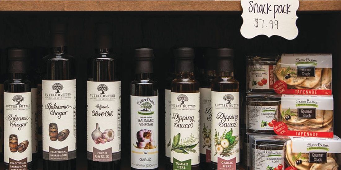 Bottles of olive oil are lined up on a shelf with a sign that says snack pack
