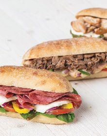 Three sandwiches are sitting on a white table.