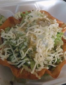 A close up of a taco with cheese and lettuce in a styrofoam container.