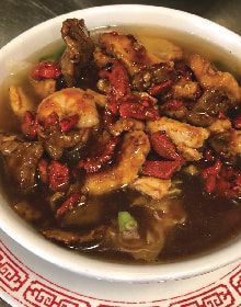 A close up of a bowl of soup with meat and shrimp.