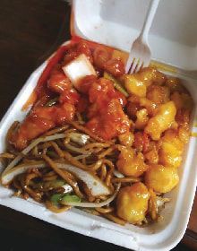 A styrofoam container filled with noodles , shrimp , and chicken with a fork in it.