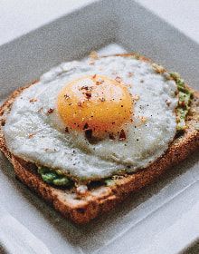 A close up of a fried egg on a piece of toast on a plate.