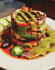 A white plate topped with a stack of vegetables and sauce.