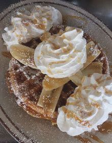 A close up of a waffle with whipped cream and bananas on a plate.