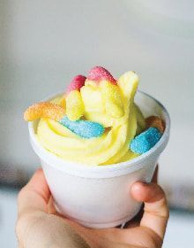 A person is holding a cup of frozen yogurt with gummy worms on top.