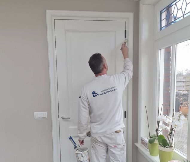 Man schildert met een kwast een wit deurkozijn in een huis.