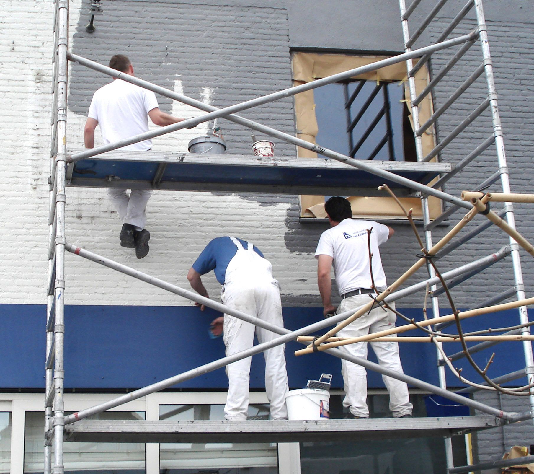 Schilders op een steiger die een buitenmuur schilderen. Blauw-witte verf, bakstenen gebouw.