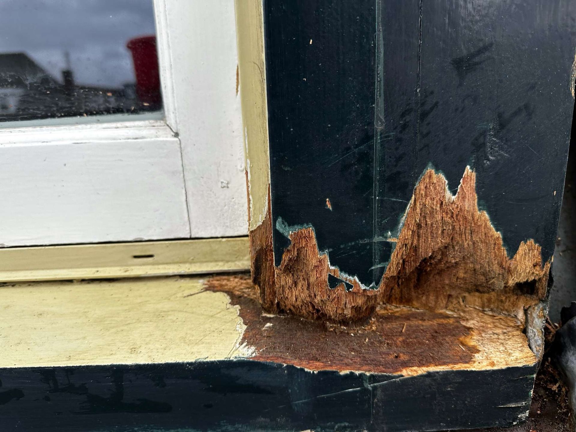 Rottend, beschadigd houten raamkozijn met afbladderende verf en zichtbaar hout.