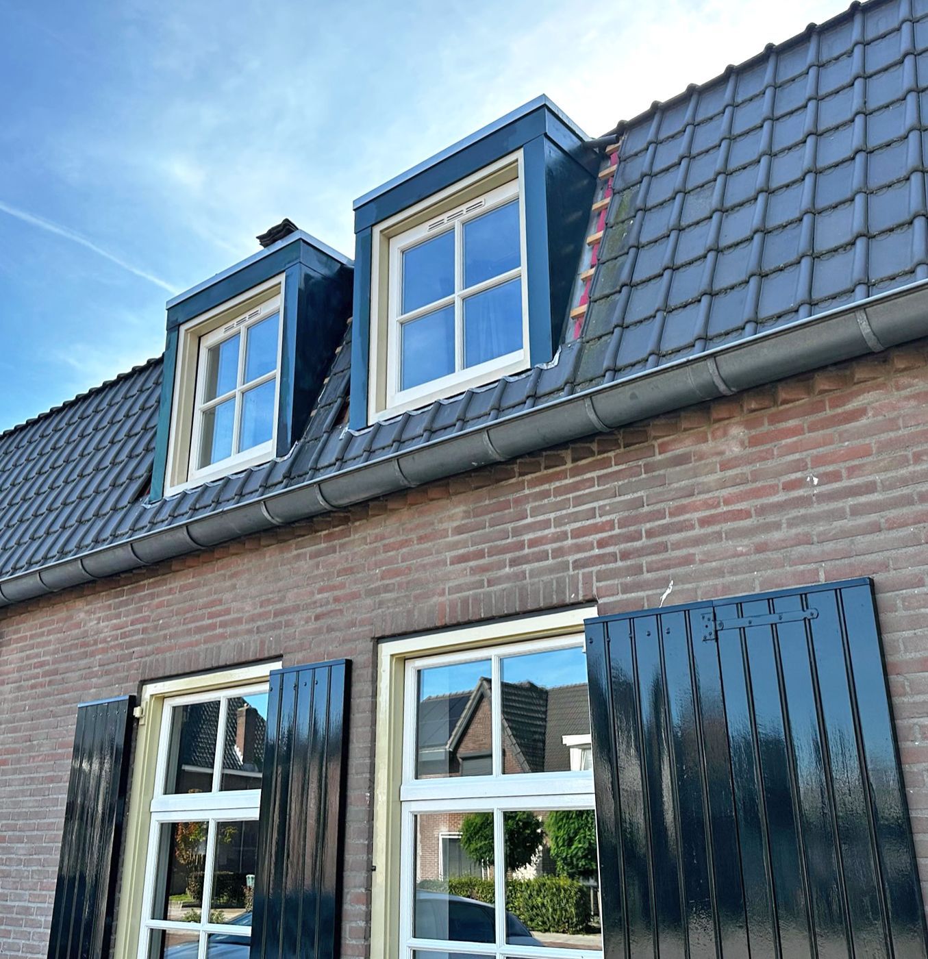 Bakstenen huis met zwarte luiken, twee dakkapellen met witte kozijnen en een donker pannendak.