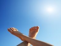 A person 's feet are crossed in front of a blue sky.
