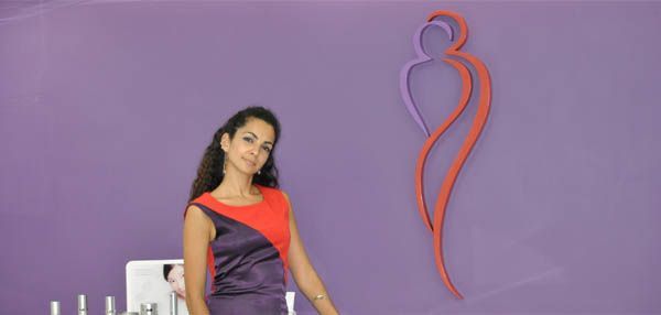 Dr Dalila Gomes in a purple dress is standing in front of a purple wall.