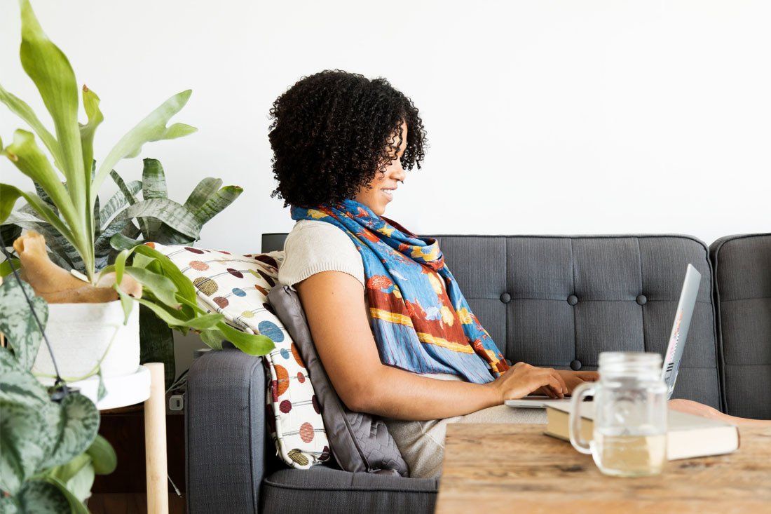 Woman is Sitting on a Couch Using a Laptop Computer — MoneySmith Group In Kingscliff, NSW