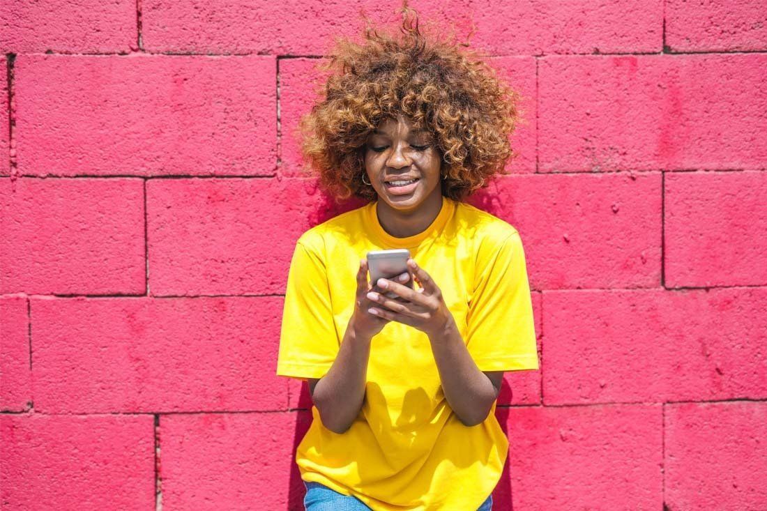 Woman is Sitting in Front of a Pink Brick Wall Using Her Cell Phone — MoneySmith Group In Kingscliff, NSW