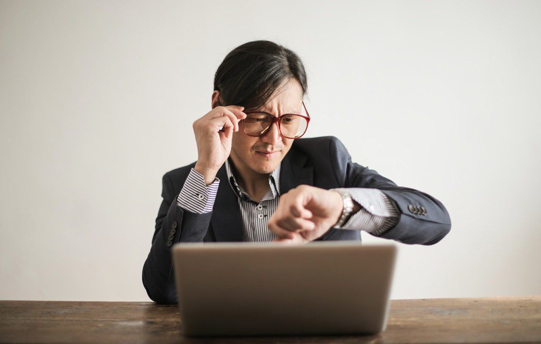 A Man is Sitting at a Desk Looking at His Watch — MoneySmith Group In Kingscliff, NSW